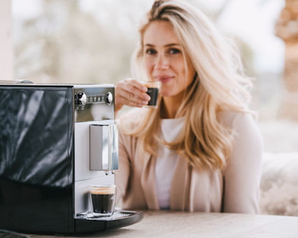 Melitta® FAM in front while blonde woman enjoys coffee in the back
